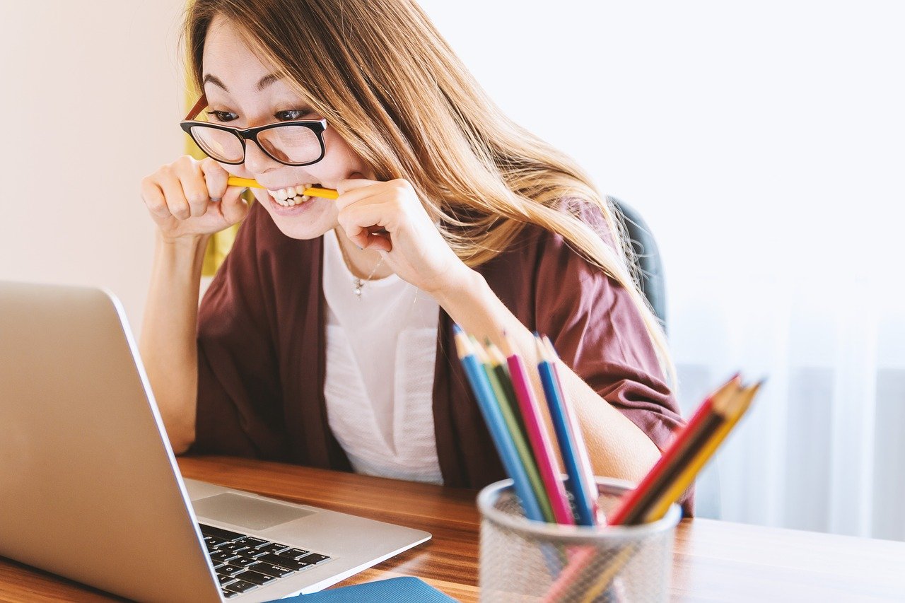 Woman biting pencil in front of laptop